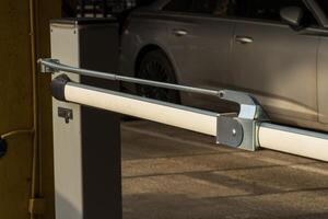 An automatic barrier gate stands closed at the entrance of a parking lot, ensuring controlled access and security for vehicles. The modern equipment enhances safety for all users photo