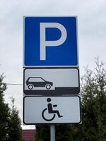 A clear parking sign stands between green shrubs, displaying a designated area for vehicles and additional space for accessible parking. It is important for guiding drivers in a busy area photo
