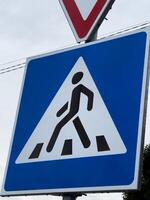 A triangular blue warning sign depicts a person walking amidst construction barriers, notifying drivers of pedestrian presence in a work zone. This sign is positioned at a busy intersection photo