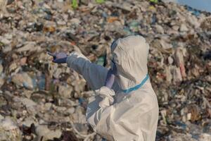 A sanitation worker in protective gear points at a towering mountain of trash at a landfill, highlighting the urgent need for waste management and recycling amid rising pollution concerns photo