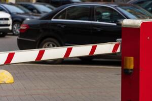 A closed automatic barrier secures the entrance to a parking lot, preventing unauthorized access. The scene captures the red and white striped gate in operation on a busy road photo
