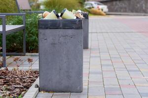 Various garbage containers are overflowing with trash bags, positioned along a clean urban walkway. The scene highlights the importance of proper waste disposal and recycling practices photo