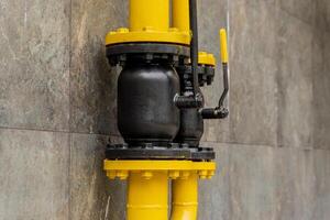 A yellow gas pipe with a black valve is mounted on a grey wall, showcasing an essential connection for transporting gas. The setup reflects modern energy infrastructure photo