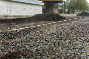 Gravel and dirt are spread along the sidewalk of an urban road in the midst of construction. Industrial buildings are present in the background as work continues photo