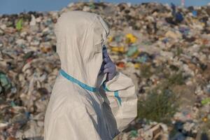 A worker in protective gear surveys a large landfill filled with trash and plastic debris, drawing attention to the pressing issues of pollution and waste management photo