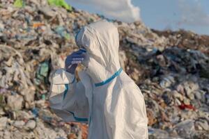A sanitation worker in protective clothing examines a large landfill overflowing with waste, emphasizing the urgent need for effective waste management and recycling efforts photo