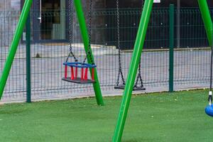 Swings stand ready for children to enjoy in a vibrant public park. The green turf and chain link fence create a safe and playful environment for outdoor fun photo