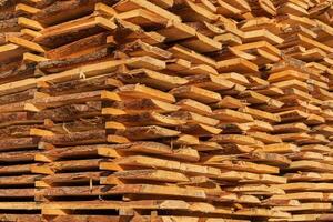 Sunlight filters through wooden stacks at a sawmill, revealing freshly cut timber planks arranged neatly. The warm tones of the wood highlight the texture, showcasing quality lumber photo