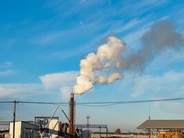 Dark smoke billows from towering smokestacks at a vast industrial facility under a clear blue sky. This setting highlights the ongoing production and pollution challenges faced by factories photo