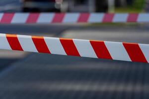 Caution tape in bright red and white stretches across a pathway in a city, signaling a warning and designating a forbidden area to ensure public safety and security photo