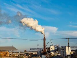 Production activities generate thick smoke from the factory's smokestacks, impacting the surrounding environment while machinery operates under a bright sky photo