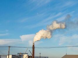 Thick smoke billows from smokestacks in an industrial area, contributing to air pollution as machinery operates beneath a clear yet cloudy sky during the day photo