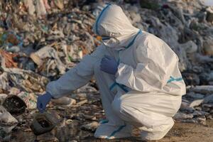 A dedicated environmentalist investigates water pollution at a waste dump site, carefully collecting samples while dressed in protective clothing during late afternoon light photo