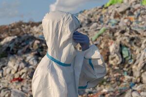 Wearing protective gear, an environmental health worker surveys a landfill overflowing with plastic waste photo