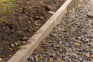 A fresh gravel path is taking shape alongside a new concrete edging. Vibrant autumn leaves lay scattered nearby, highlighting a peaceful outdoor project in progress photo
