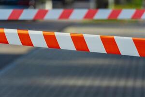 Caution tape stretches across a pathway, creating a vibrant barrier that signals restricted access. Sunlight shines brightly, illuminating the bold orange and white stripes, enhancing visibility photo