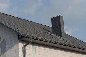 A modern roof showcases sleek shingles and a contemporary chimney against a blue sky, indicating recent construction work. The contrasting textures highlight excellent craftsmanship photo