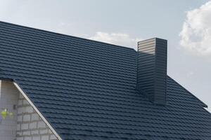 A beautiful modern house boasts a stylish dark slate roof, highlighting the clean lines and architectural design. Sunlight reflects off the roof shingles as clouds drift lazily photo