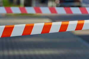 Bright orange and white caution tape flutters lightly in the breeze, marking off a busy street. The tape serves as a clear warning and adds a pop of color to the surrounding pavement and buildings photo