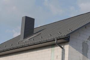 A stylish rooftop highlights contemporary architecture, featuring a prominent chimney and elegant shingles. The bright sky adds a sense of openness and tranquility, enhancing the overall aesthetic photo