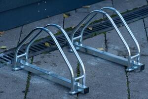 Two sleek and sturdy bicycle racks are positioned on a clean concrete sidewalk. Leaves are scattered nearby, hinting at the changing seasons and adding a touch of nature to the urban setting photo