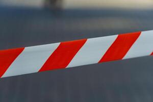 A striking pattern of red and white caution tape stretches across an open area, signaling restricted access while brightly contrasting with the surrounding environment on a sunny day photo