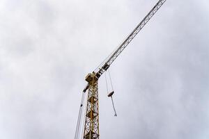 A towering yellow crane stands against an overcast sky, lifting heavy materials at a bustling construction site, symbolizing progress and ingenuity in urban development photo