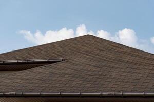 A beautifully crafted roof showcases its unique texture against the backdrop of a clear blue sky, with gentle white clouds drifting by, highlighting a calm atmosphere photo