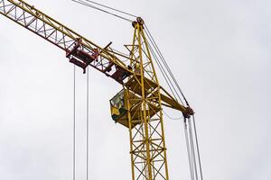 A tall yellow crane stands prominently against a gray sky, while workers maneuver materials at a construction site, showcasing urban development and labor in action photo