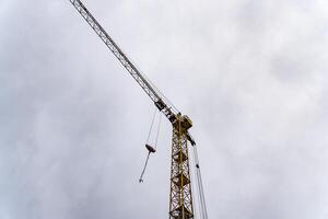 A tall construction crane looms over the skyline, its yellow structure contrasting with the grey clouds. It is actively involved in lifting materials for a new building project photo