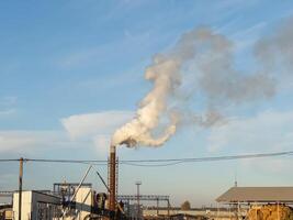 In the heart of a manufacturing district, thick smoke streams from tall chimneys, contrasting with the serene blue sky. It captures the essence of industrial activity and progress photo