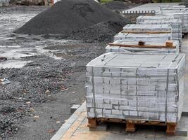 Crates stacked high with gray concrete blocks are neatly arranged on pallets, ready for use in construction at a bustling site in the early hours of the day photo