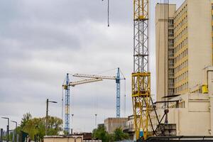 Amidst a moody sky, towering cranes stand vigil over a busy urban construction site, where workers bustle about, shaping the future of the city photo