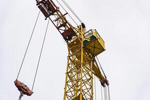 A tall yellow construction crane reaches skyward, its sturdy frame standing out against the overcast sky, showcasing the strength of modern engineering in urban development photo