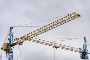 Massive construction cranes stretch towards the overcast sky, showcasing their intricate structure. They are pivotal in shaping the evolving city landscape, highlighting industrial progress photo