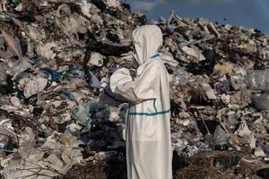 Dressed in a protective suit, the worker surveys the expansive landfill filled with discarded items, emphasizing the urgent need for sustainable waste management initiatives photo