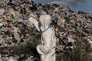 The worker, clad in a protective suit, surveys the vast expanse of a landfill. As he gestures towards the mountains of refuse, concerns about environmental impact and waste management arise photo
