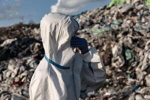 Dressed in a protective suit, a worker stands at a landfill, reflecting on the scale of waste surrounding them, emphasizing the importance of responsible waste management photo