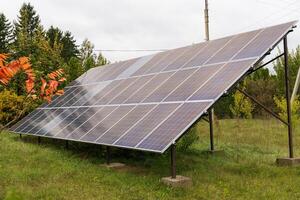 A large solar panel array is set up on a grassy field, angled towards the sky. Trees surround the panel photo