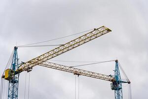 Two towering construction cranes are actively engaged in the building process of a new house, surrounded by a cloudy sky in the early morning photo
