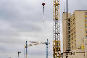 Several construction cranes are busy lifting materials at a house construction site located in a bustling urban environment during overcast weather photo