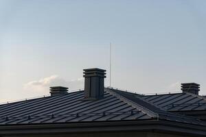 The roof showcases sleek metal tiles, creating a contemporary appearance. Two prominent chimneys rise from the structure, blending modern aesthetics with functionality photo