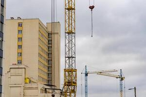 Construction cranes are actively lifting materials for a new house in an urban setting, showcasing the progress in residential development under gray skies photo