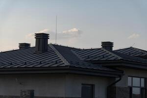 This rooftop features sleek metal tiles and multiple chimneys, emphasizing a modern architectural style. The backdrop includes a calming evening sky, enhancing the aesthetic appeal photo