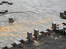 Workers are in the process of laying brick pavers to create a new sidewalk. The area shows scattered pavers and construction materials, indicating ongoing work photo
