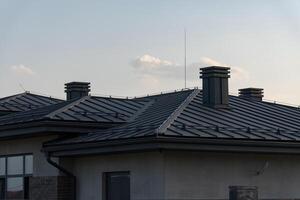 The image showcases a modern rooftop featuring slanted metal roofing and neatly arranged chimneys under a sunny sky, highlighting its construction and design elements photo
