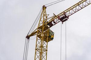 The crane is actively lifting heavy materials above a construction site, with workers visible in the cab, showcasing their work during overcast weather photo