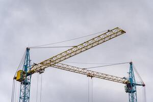 Two large construction cranes dominate the skyline, their bright yellow and blue colors contrasting against the overcast sky photo