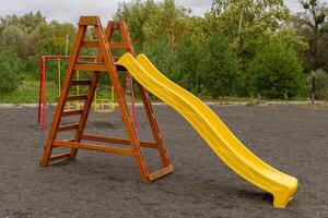Children enjoy swinging on colorful play equipment in a community playground, surrounded by greenery, on a cloudy afternoon. Their laughter fills the air photo