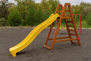 Joyful children enjoy swinging back and forth on playground swings, surrounded by lush trees and a bright sky, while a colorful slide stands nearby photo